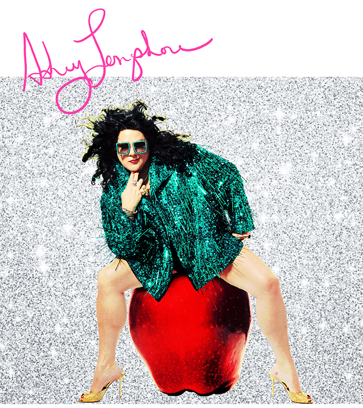 Pop artist Ashley Longshore wearing a green sequined jacket and seated atop a giant apple against a silver glitter background. Artist, painter, sculptor, creator.