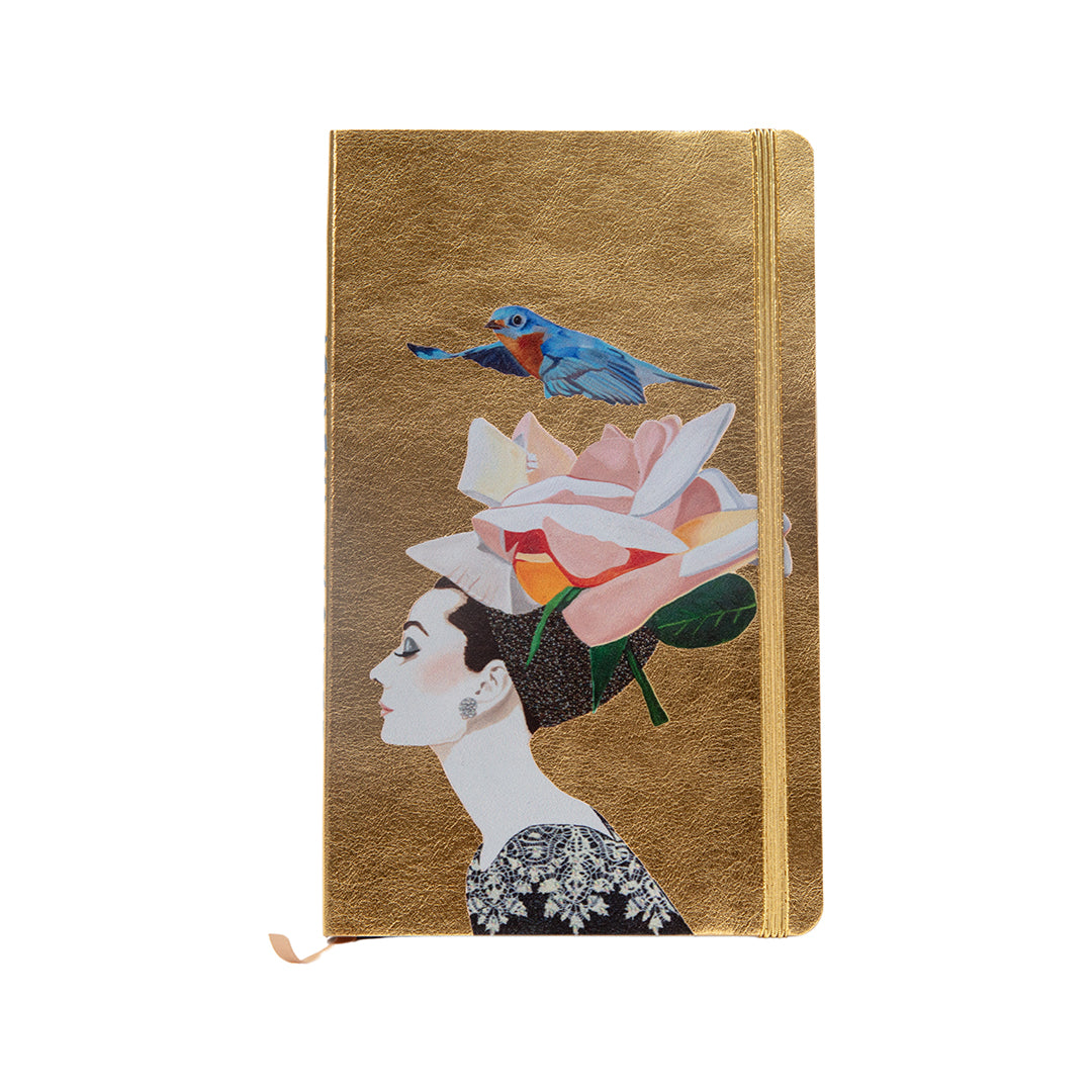 Gold metallic journal featuring Ashley Longshore’s artwork of a woman in profile with a floral headpiece and a bluebird above her head.