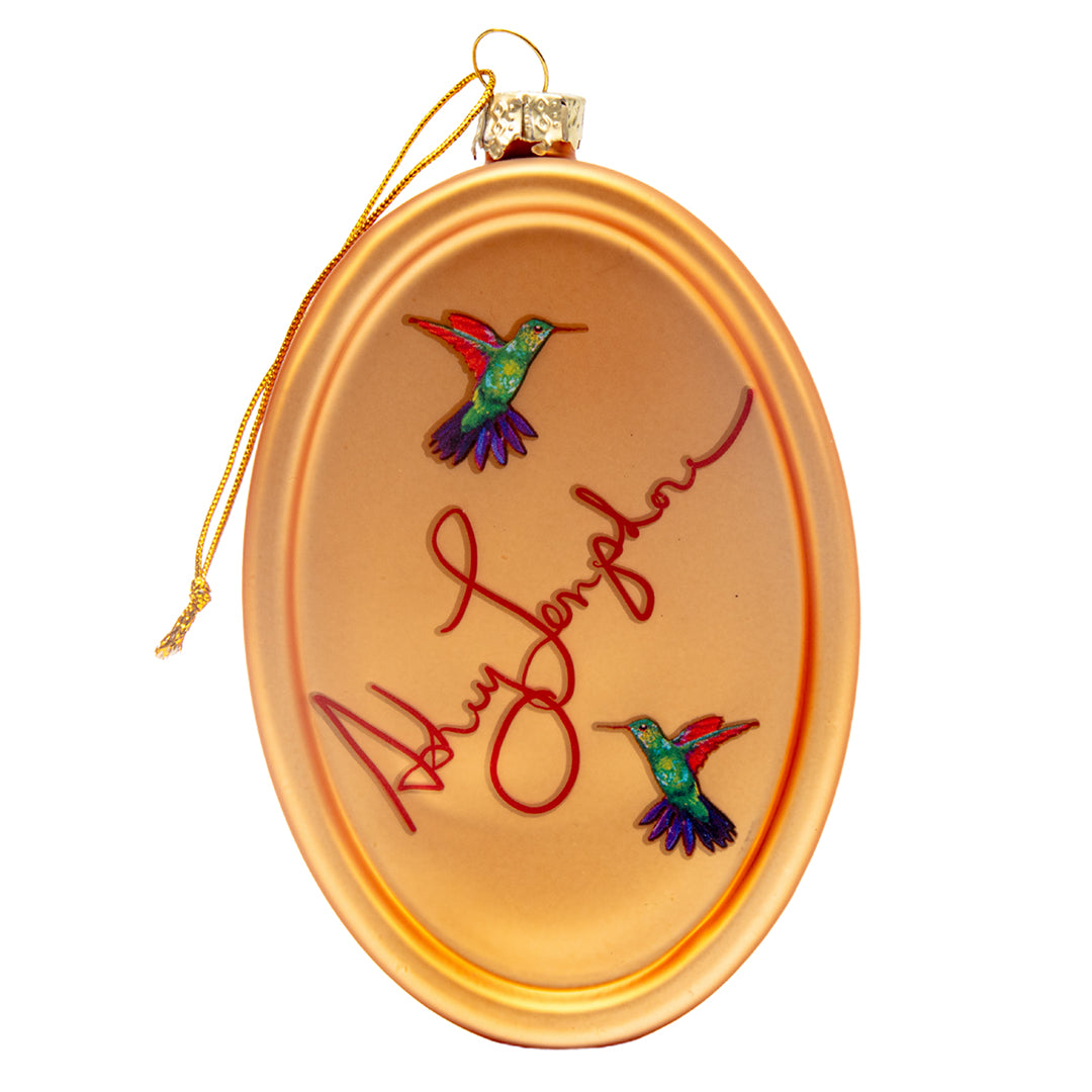 Back of ornament showing Ashley Longshore’s signature and two colorful hummingbirds on a metallic gold finish.