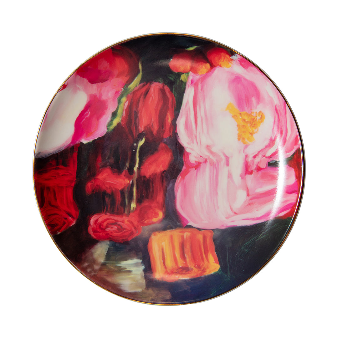 Porcelain dessert plate with pink and orange floral design against a dark background and gold trim.
