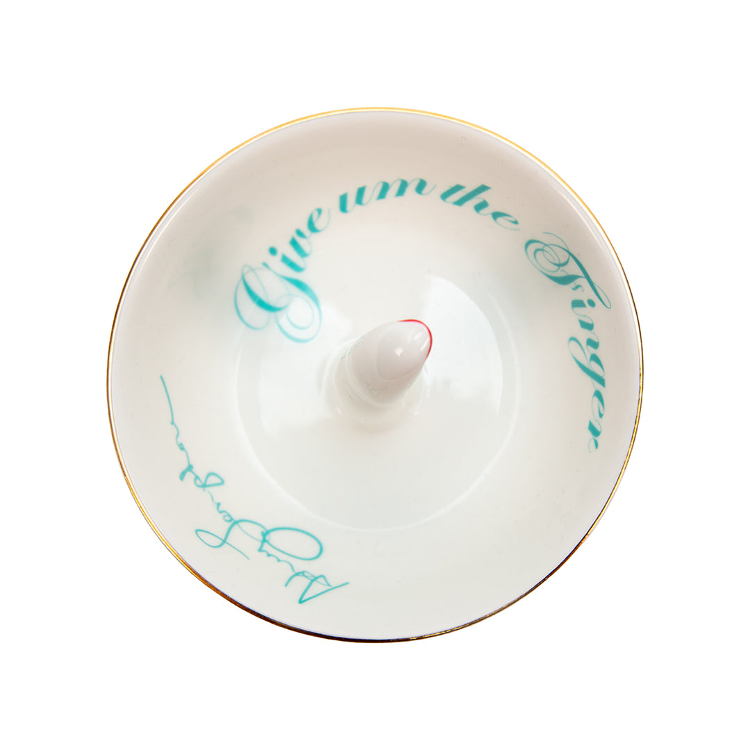 Ashley Longshore porcelain middle finger ring dish with red nail and turquoise script text reading “Give Um the Finger” along with Ashley Longshore’s signature.
