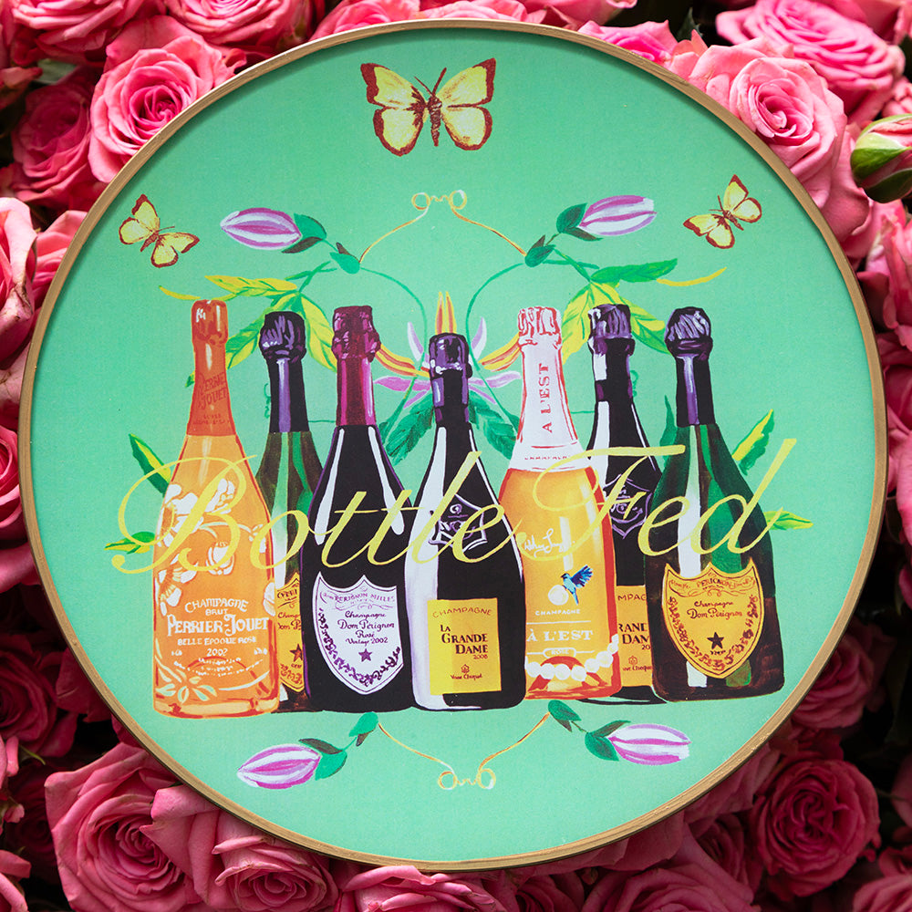 7-inch round glass tray with jade green background featuring illustrated champagne bottles, butterflies, floral accents, and the words “Bottle Fed” in script across the front.