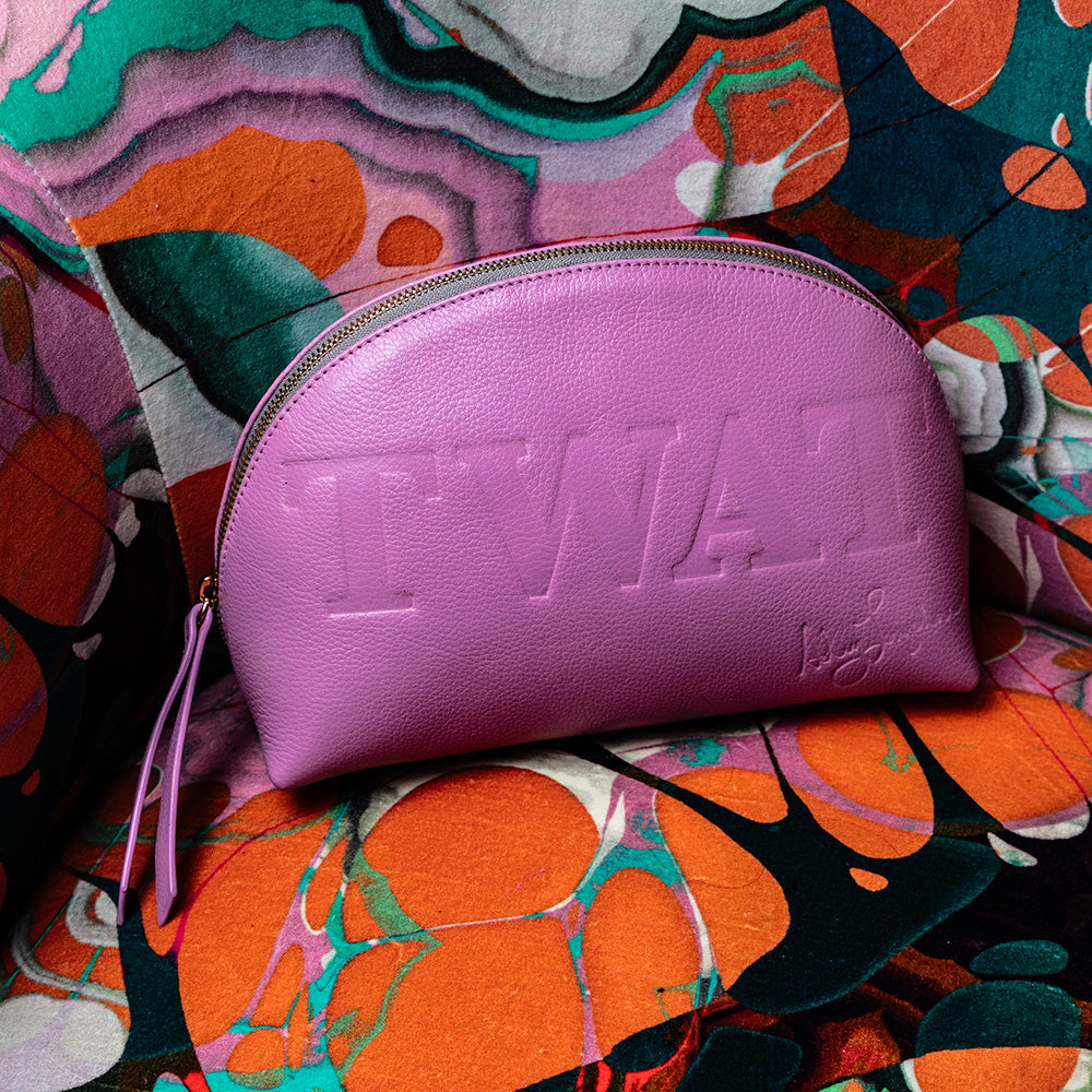Barbie pink leather Ashley Longshore pouch embossed with bold lettering, displayed on a colorful patterned chair.