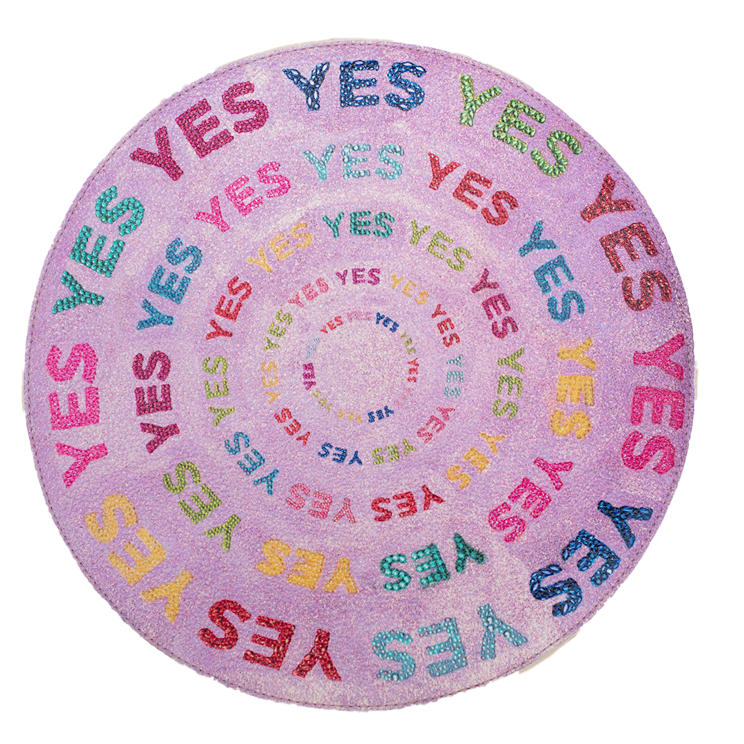 A circular vegan leather clutch bag with the word 'YES' written in multiple colors on a purple background, featuring a contrasting zipper and a signature on the back.