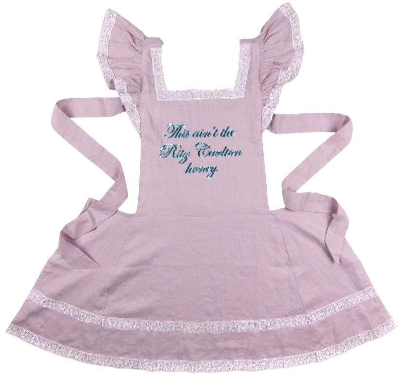 I made a fucking apron just for YOU!!! "This Ain't The Ritz Carlton Honey." This kitchen ain't a damn hotel. Kick your feet up and pour yourself a DRINK!! This apron is GORGEOUS. It's sequined, ruffled and trimmed with iridescent white sequin lace!!! I love it!! Get you one before it's gone... this baby is super limited!! *One size fits all.. This apron is hand embroidered pink linen with hand sequined details. Dry Clean Only, Lightweight & Lined Linen Fabric, Ashley Longshore Signature Loop Tag.